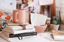 light brown ceramic coffee mug on stack of books on cluttered shelf