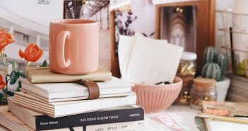 light brown ceramic coffee mug on stack of books on cluttered shelf