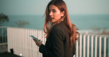 pretty woman with long brown hair holding smartphone and looking back over her shoulder