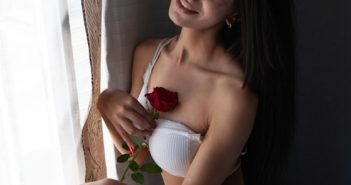 closeup of a red rose held by a beautiful brunette woman wearing a sexy white bra with a strap down