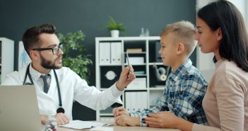 doctor examining young boy with attractive mother looking on