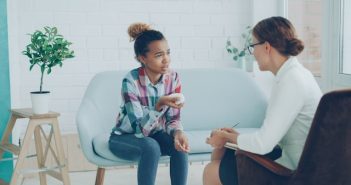 teenage girl sitting on couch talking to a female therapist