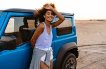Photo of an african american woman standing at her car on beach at sunrise