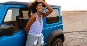 Photo of an african american woman standing at her car on beach at sunrise