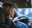 over shoulder view of blonde woman driving car holding steerring wheel