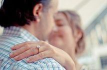 man and woman embracing with woman's hand on his shoulder with engagement ring