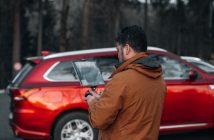man with laptop by red car