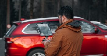 man with laptop by red car