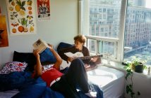 two guys sitting on bed one playing guitar