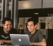 two men working at desk with laptop