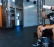 man in gym sitting on bench drinking from water bottle