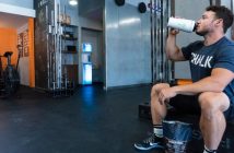 man in gym sitting on bench drinking from water bottle
