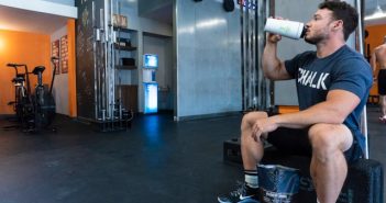 man in gym sitting on bench drinking from water bottle