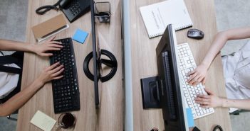 overhead shot of office workers at desk working on PCs