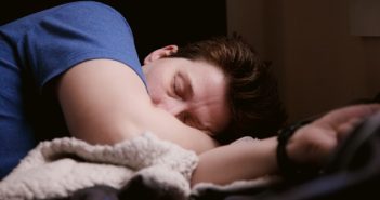 man sleeping in bed with blue shirt and white sheets