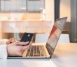 Person seated at a table using a laptop and holding a credit card while shopping online at home