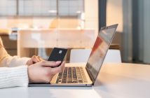 Person seated at a table using a laptop and holding a credit card while shopping online at home