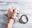 hand with handcuffs and cash money on table