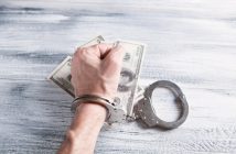 hand with handcuffs and cash money on table
