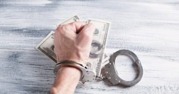 hand with handcuffs and cash money on table
