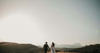 bride and groom holding hands in outdoor setting rear view