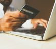 man holding credit card while typing into laptop