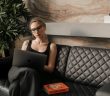 pretty blonde professional woman on couch using laptop with book next to her on couch